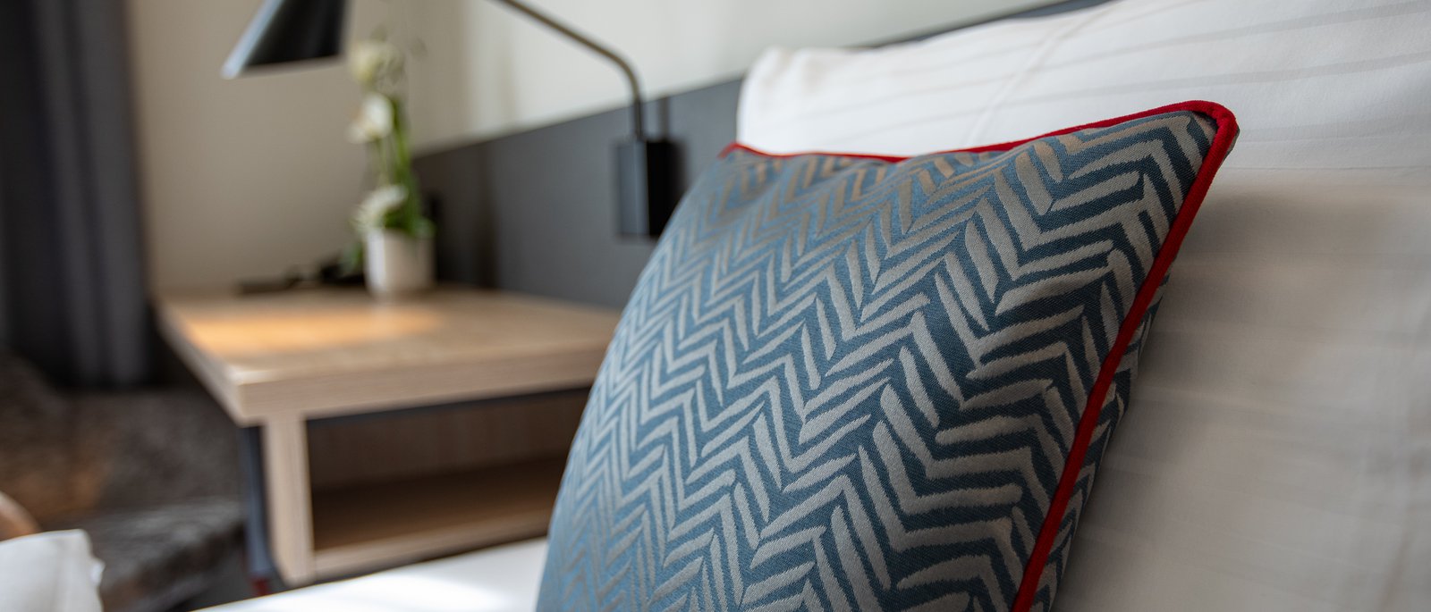 Single room Blue patterned pillow with red trim on a white bed in a hotel room