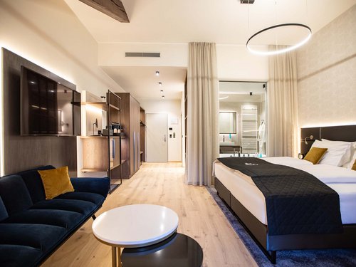 Single room Modern hotel room with large bed, sofa, TV, and light wooden flooring